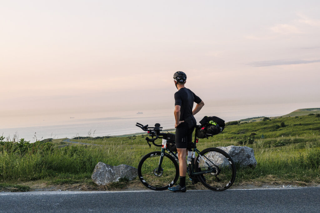 A man on his bike during an ultracycling event, looking out over the ocean during a break.